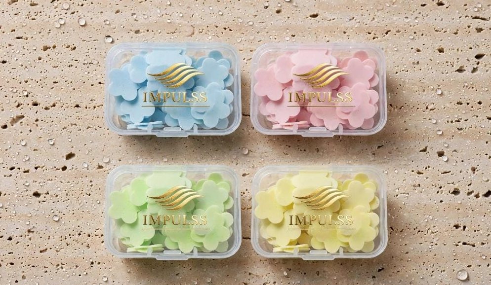 Cuatro cajas de jabón en forma de flor IMPULSS Flor en azul, rosa, verde y amarillo sobre travertino
